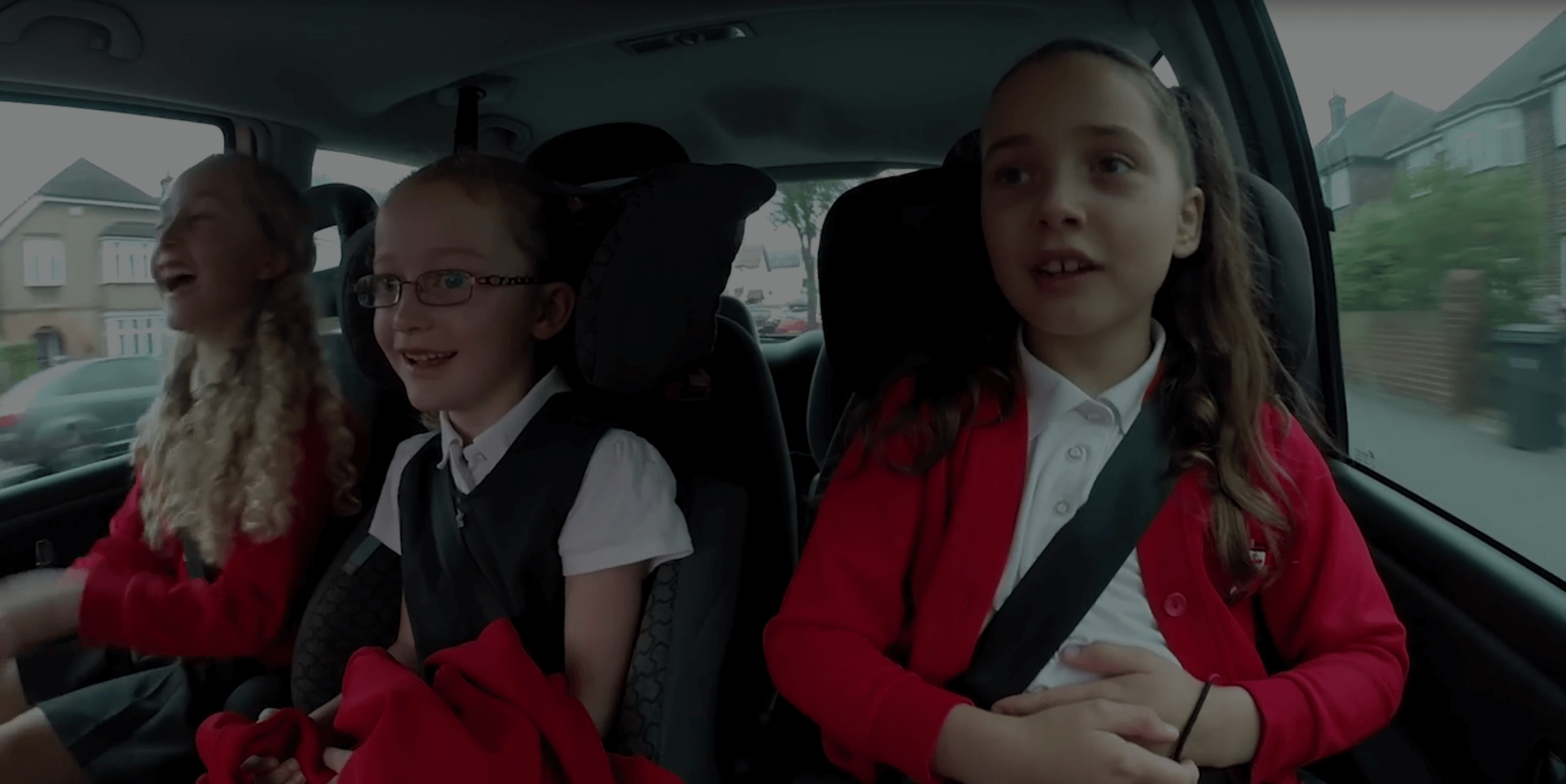 three girls in school uniforms sitting in back seat of car
