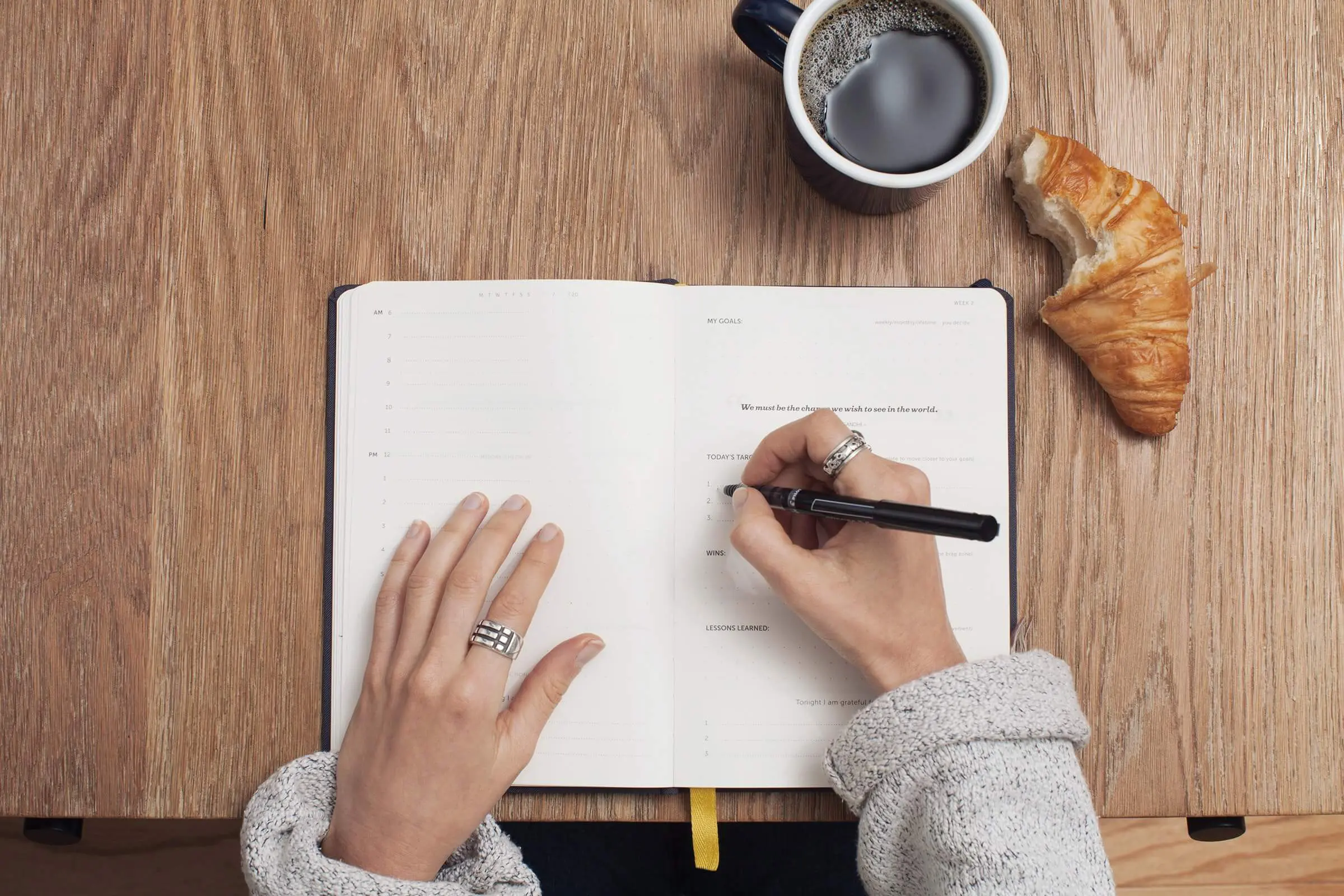 writing in journal with coffee and pastry on table