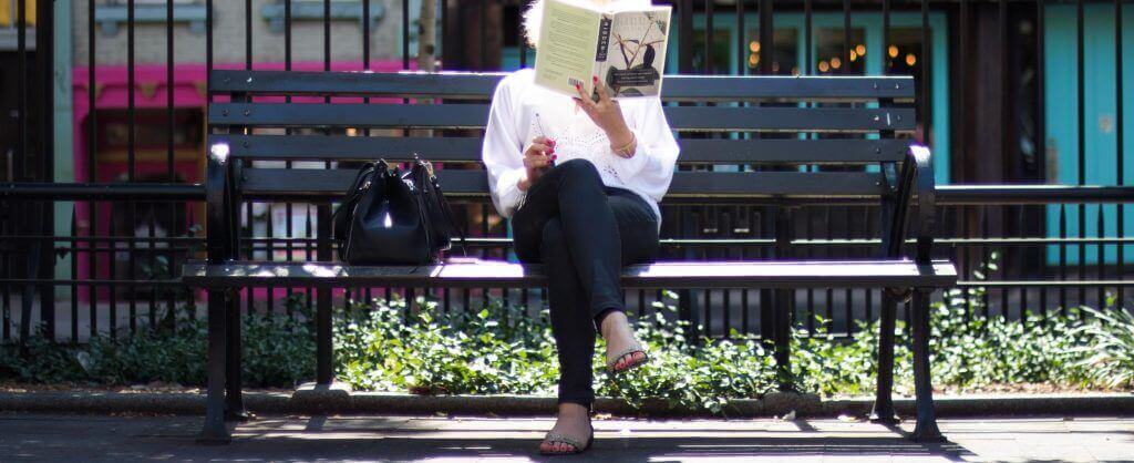femme lisant un livre sur un banc public
