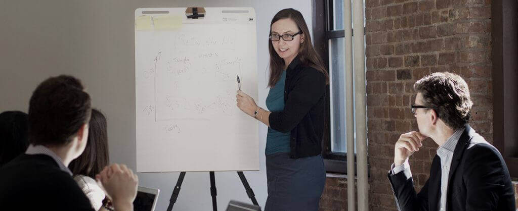woman presenting on whiteboard with coworkers watching