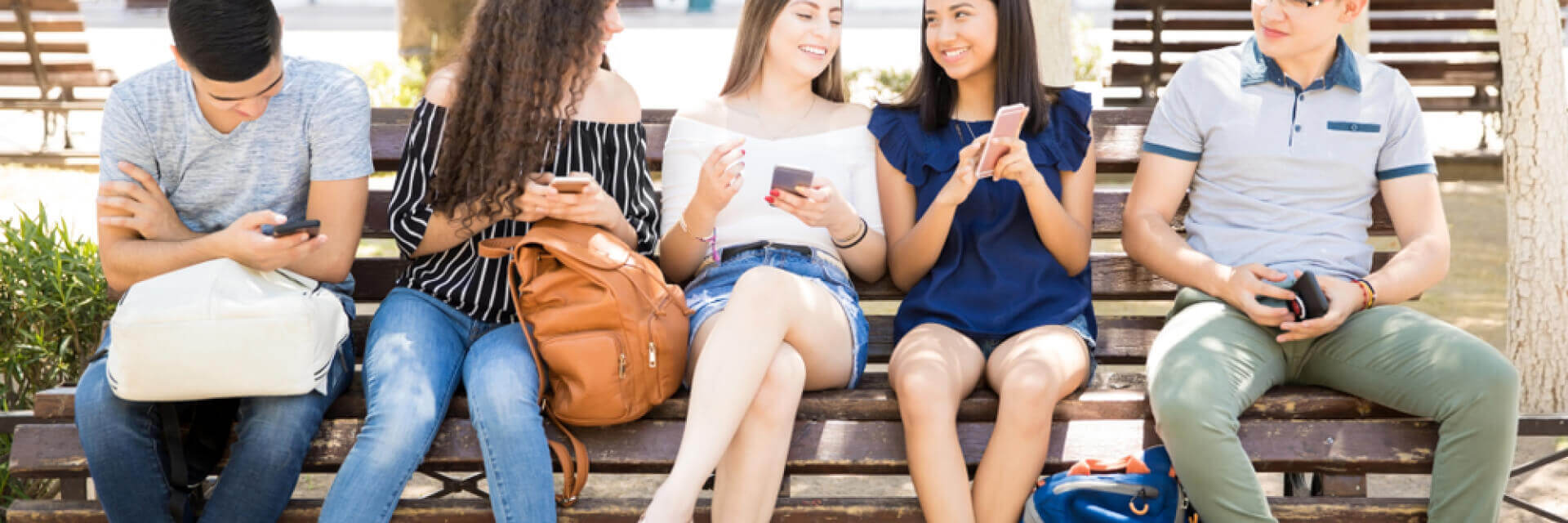 a group of people sitting on a bench looking at their phones