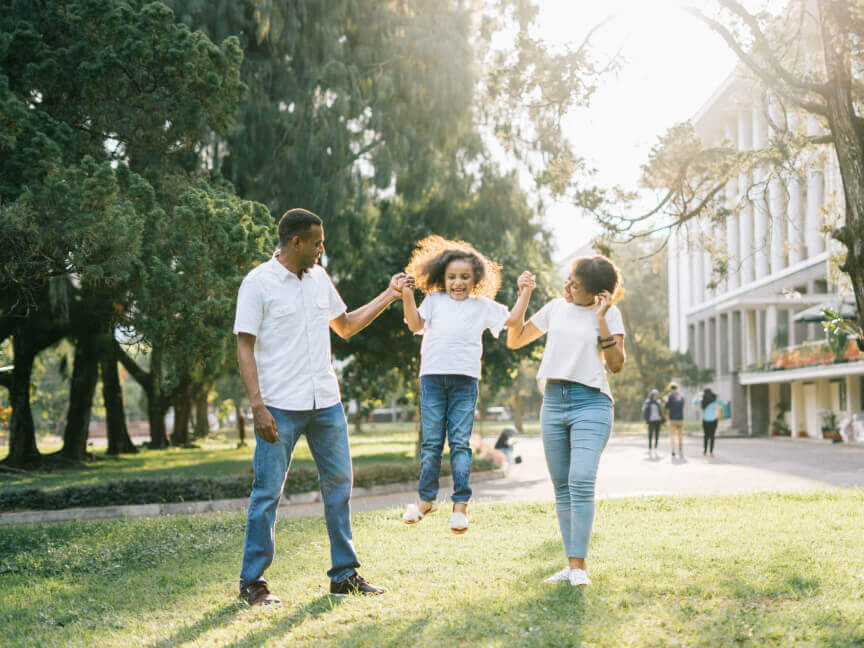 a family is holding hands and jumping in the air in a park .