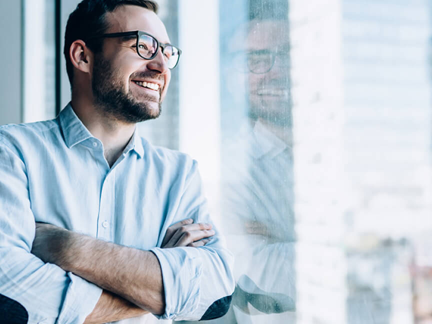 a man with glasses is smiling and looking out a window