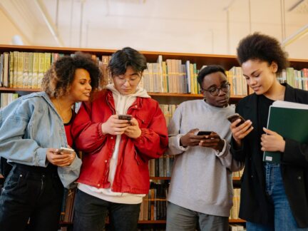 Four young students in a library looking at their smartphones, illustrating Gen Z product discovery through AI assistants